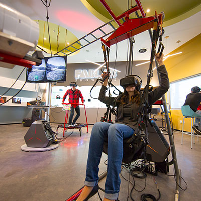 Student in foreground sitting in a VR harness and headset while another student in background stands up while wearing VR headset