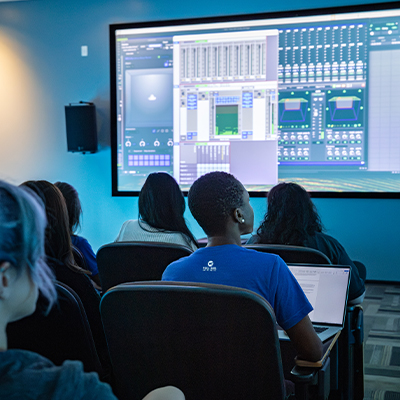 Students in looking at a large screen of the op board in Full Sail's Dolby Atmos studio