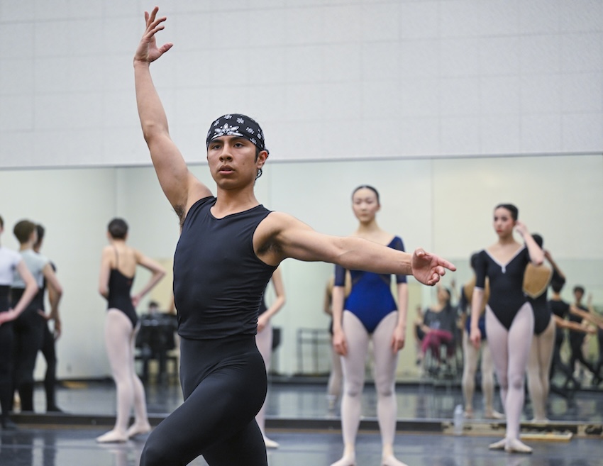 A dancer holds a pose while two other dancers observe behind him